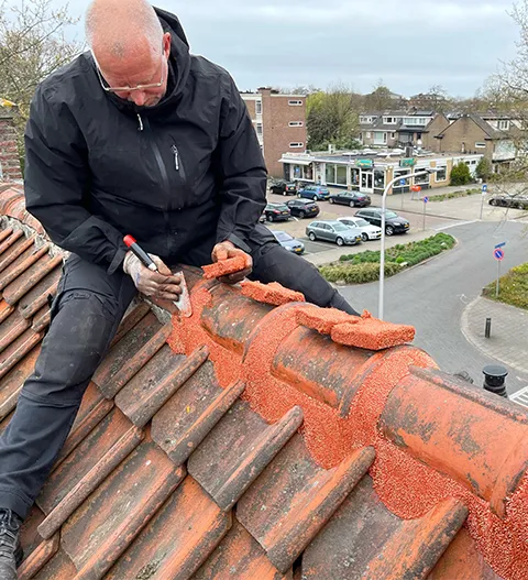 nokvorsten-repareren-op-een-dak Lorje repareert de nokvorsten van een oranje dak